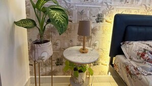 Ein Schlafzimmer mit einem Bett, einem runden Tisch mit Lampe und zwei Zimmerpflanzen.
