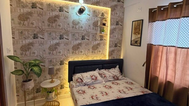 Ein Schlafzimmer mit einem Bett, einem Deckenventilator, einer an der Wand befestigten Ablage mit Pflanzen und einer Wandtapete mit Muster.
