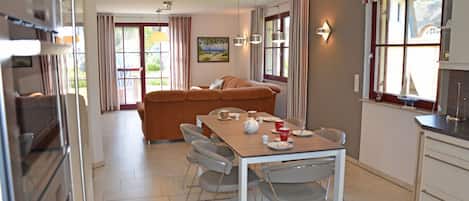 Un comedor con una mesa preparada para cuatro personas, un sofá y una cocina con armarios y una ventana.
