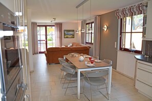 Zona pranzo con tavolo imbandito per quattro persone, divano e angolo cottura con pensili e una finestra.