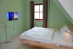 A single bed with a wooden frame, a television mounted on the wall, and a window with curtains. - Luxurious thatched-roof vacation home, about 500 m from the sandy beach, with a fireplace and sauna (Glowe)