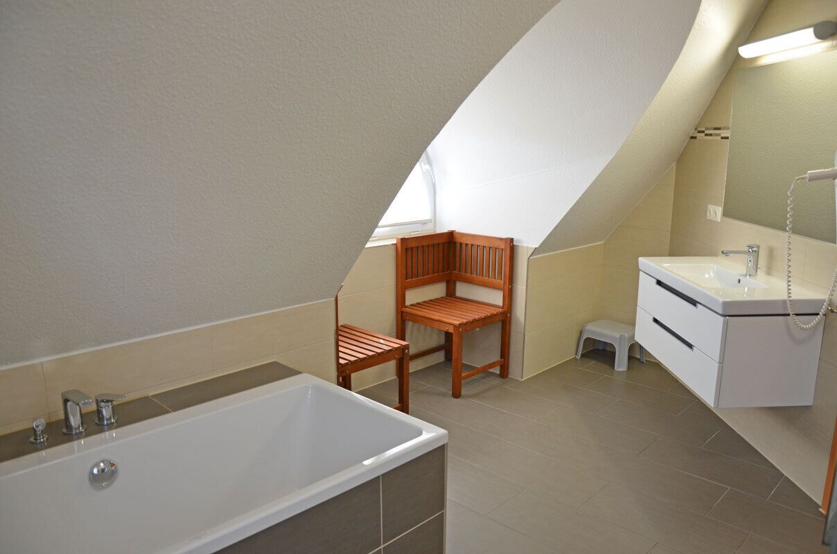 Une salle de bain avec une baignoire, une chaise en bois, un lavabo et un miroir.