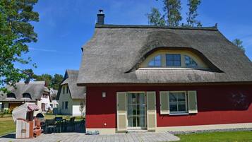 A traditional thatched-roof house with a red facade and a small patio area.