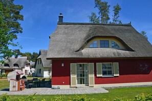 Une maison traditionnelle à toit de chaume, avec une façade rouge et un petit patio.