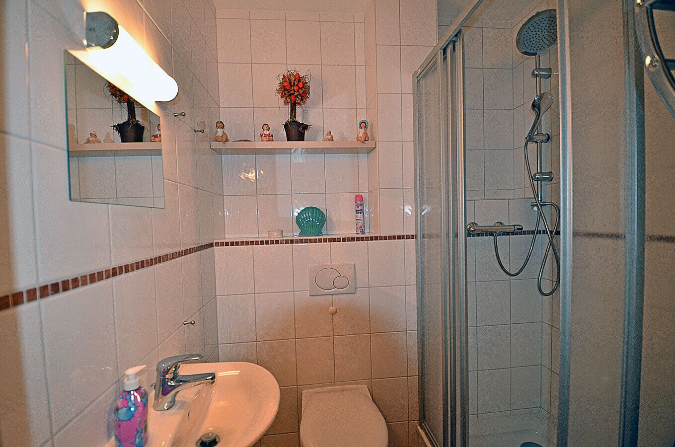 Une salle de bain équipée d’un lavabo, de toilettes, d’une douche et d’étagères où sont disposés des objets décoratifs.