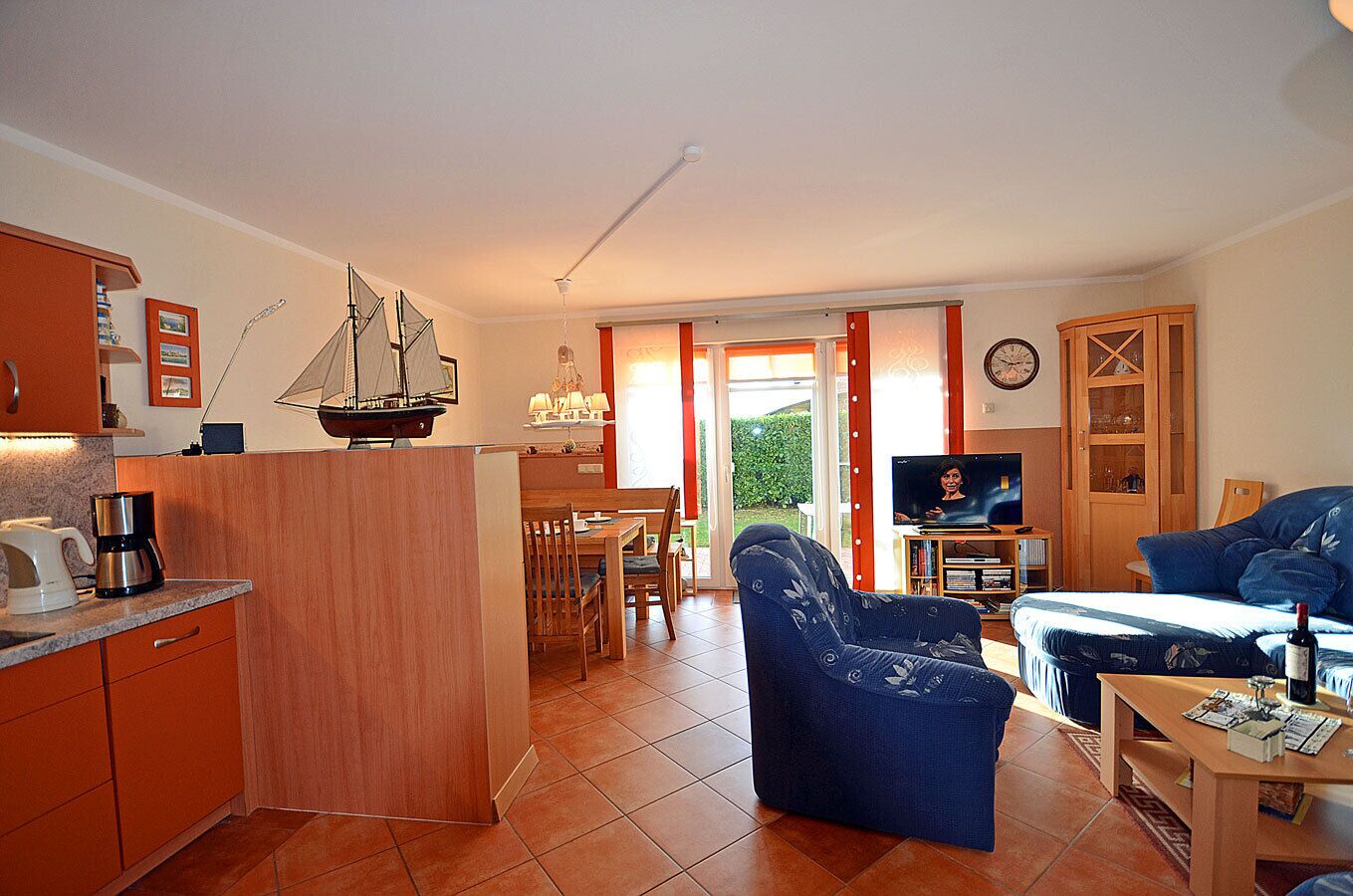 A compact living space with a kitchenette, a dining area, a seating area with a sofa and armchair, and a television.