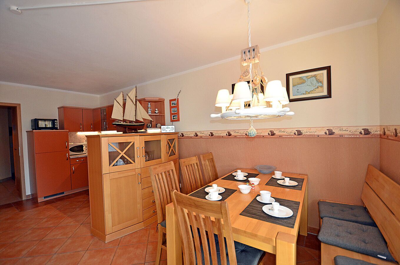 A dining area with a wooden table set for four, a kitchen with orange cabinets, and a hanging light fixture above the table.