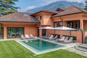 A two-story building with a swimming pool, lounge chairs, and a mountain backdrop. - Charming Lake Front Villa Beatrice in Mandello del Lario (Mandello del Lario)