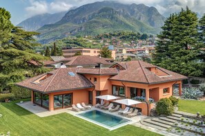Een moderne villa met een zwembad, omgeven door weelderige begroeiing en bergen op de achtergrond.