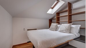 Una camera da letto con un lucernario, un letto con biancheria da letto bianca e una testiera in legno.