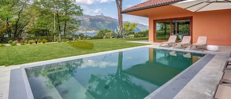 Una piscina con agua cristalina, rodeada de un césped cuidado y árboles.