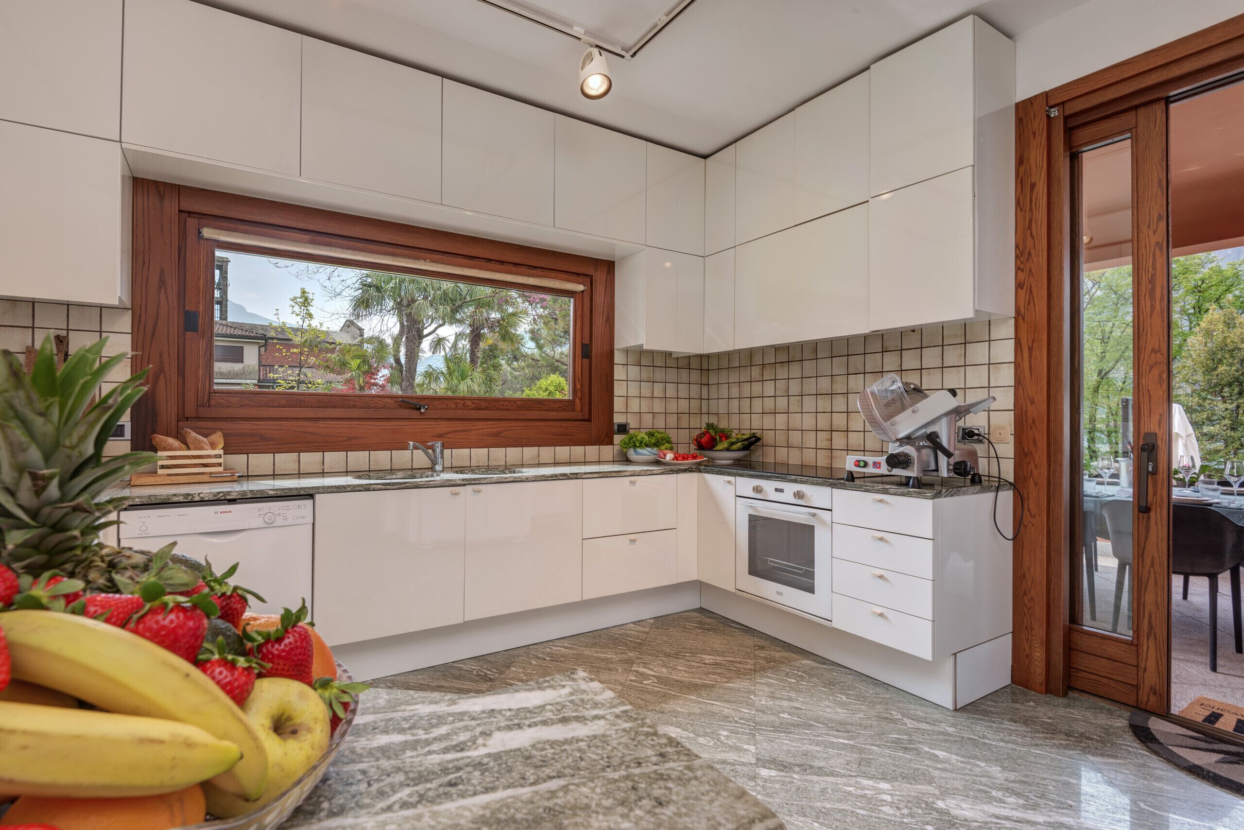 Eine moderne Küche mit weißen Schränken, einem Einbauofen und einem Fenster mit Blick auf einen Garten.