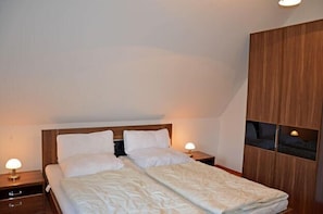 A bedroom with a double bed, two bedside tables, and a wooden wardrobe. - Vacation home with a fireplace, about 400 meters from the sandy beach, Wi-Fi, dogs welcome (Glowe)
