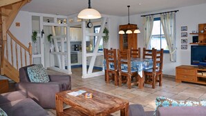 A living room with a sofa, a wooden coffee table, and a dining area with a table and chairs. - Vacation home with a fireplace, about 400 meters from the sandy beach, Wi-Fi, dogs welcome (Glowe)