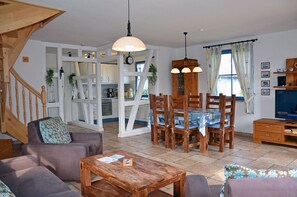 A living room with a sofa, a wooden coffee table, and a dining area with a table and chairs. - Vacation home with a fireplace, about 400 meters from the sandy beach, Wi-Fi, dogs welcome (Glowe)