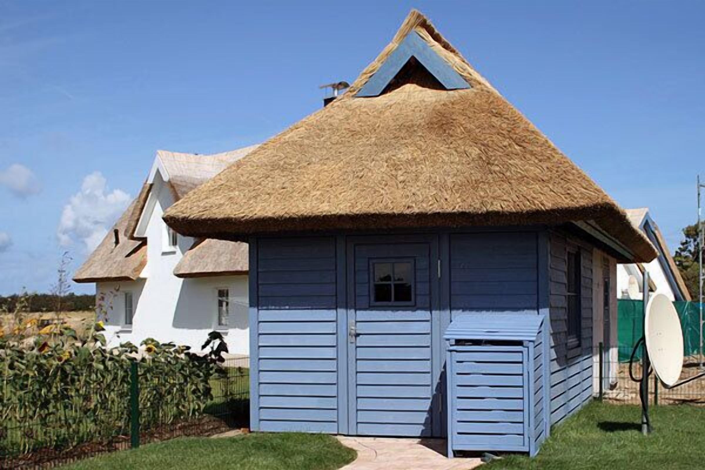 A thatched-roof house with a blue exterior, a satellite dish, and a clear sky.