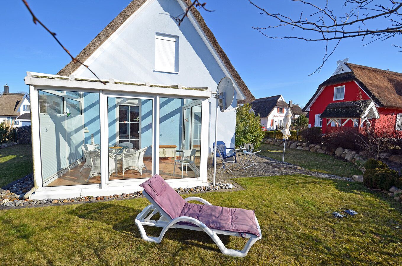 A house with a glass conservatory, a lounge chair, and a red building in the background.
