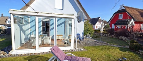 A house with a glass conservatory, a lounge chair, and a red building in the background.