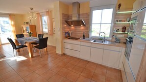 A modern kitchen with a dining area, featuring a central island, built-in appliances, and a large window providing natural light. - Quiet, central location, about 250 m from the Baltic Sea beach, sunroom (Glowe)