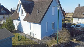 A white house with a steeply pitched roof, a visible chimney, and a small garden area with a fence. - Quiet, central location, about 250 m from the Baltic Sea beach, sunroom (Glowe)