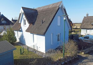 Ein weißes Haus mit einem steilen Dach, einem sichtbaren Schornstein und einem kleinen Garten mit Zäun.