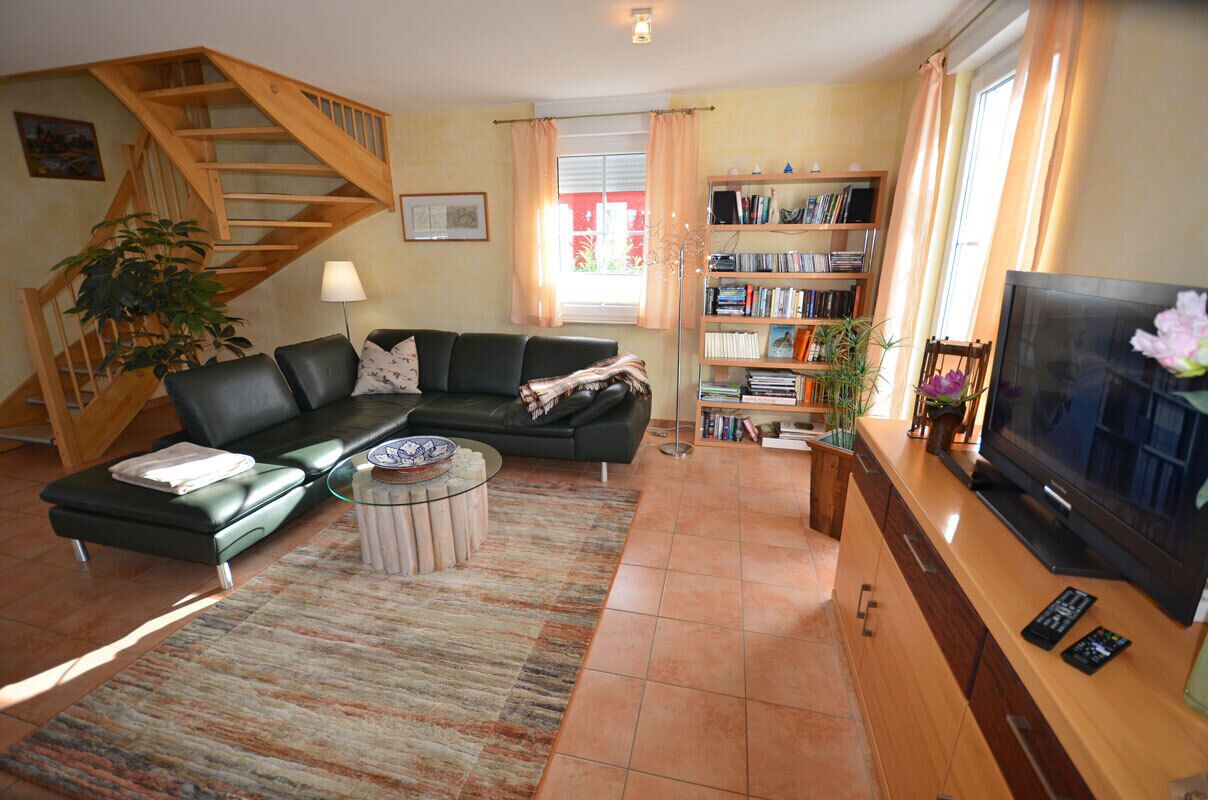 A living room with a sofa, coffee table, bookshelf, TV, and a staircase.