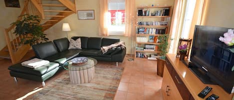A living room with a sofa, coffee table, bookshelf, TV, and a staircase.