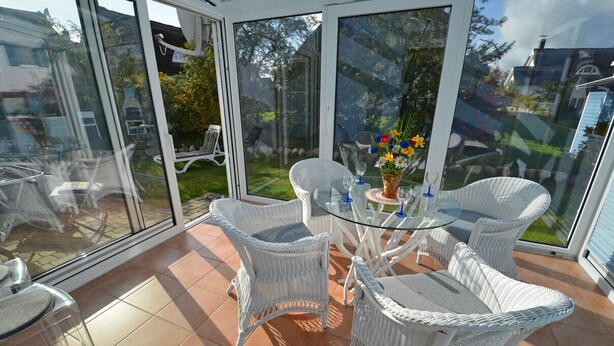 A glass-enclosed patio with wicker furniture and a glass table, overlooking a garden. - Quiet, central location, about 250 m from the Baltic Sea beach, sunroom (Glowe)