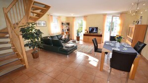 A living room with a staircase, a sofa, a dining table with chairs, a television, and a bookshelf. - Quiet, central location, about 250 m from the Baltic Sea beach, sunroom (Glowe)