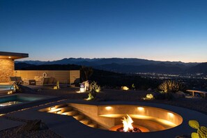 Un espace piscine extérieur moderne, doté d’un foyer, de sièges et offrant une vue sur les montagnes lointaines.