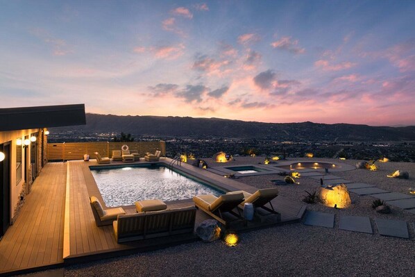 Zona de piscina en la azotea con sillones de descanso y vistas a un paisaje urbano al atardecer.