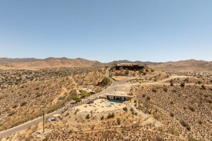 A desert landscape with a large building on a hill, a swimming pool, and a road leading to it. - Rattlesnake Ranch - Hollywood Retreat w Pool&Views (Yucca Valley)