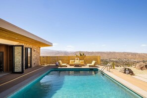 Una piscina con vista a las montañas, una terraza de madera y mobiliario exterior.