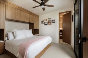 Un dormitorio con cama, ventilador de techo, armarios de madera y puerta que da a un baño.