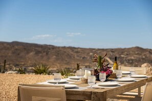 Mesa de comedor al aire libre con platos, vasos y una botella, con un paisaje desértico de fondo.