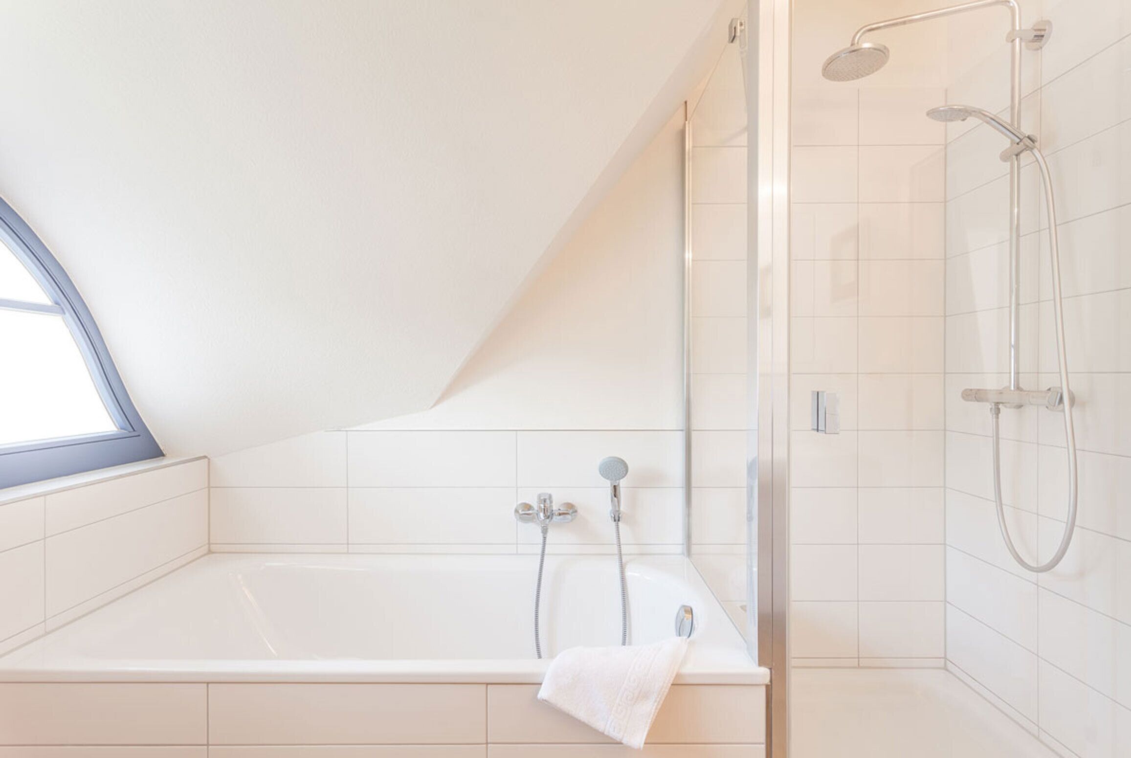 A modern bathroom with a bathtub, shower, and a skylight.