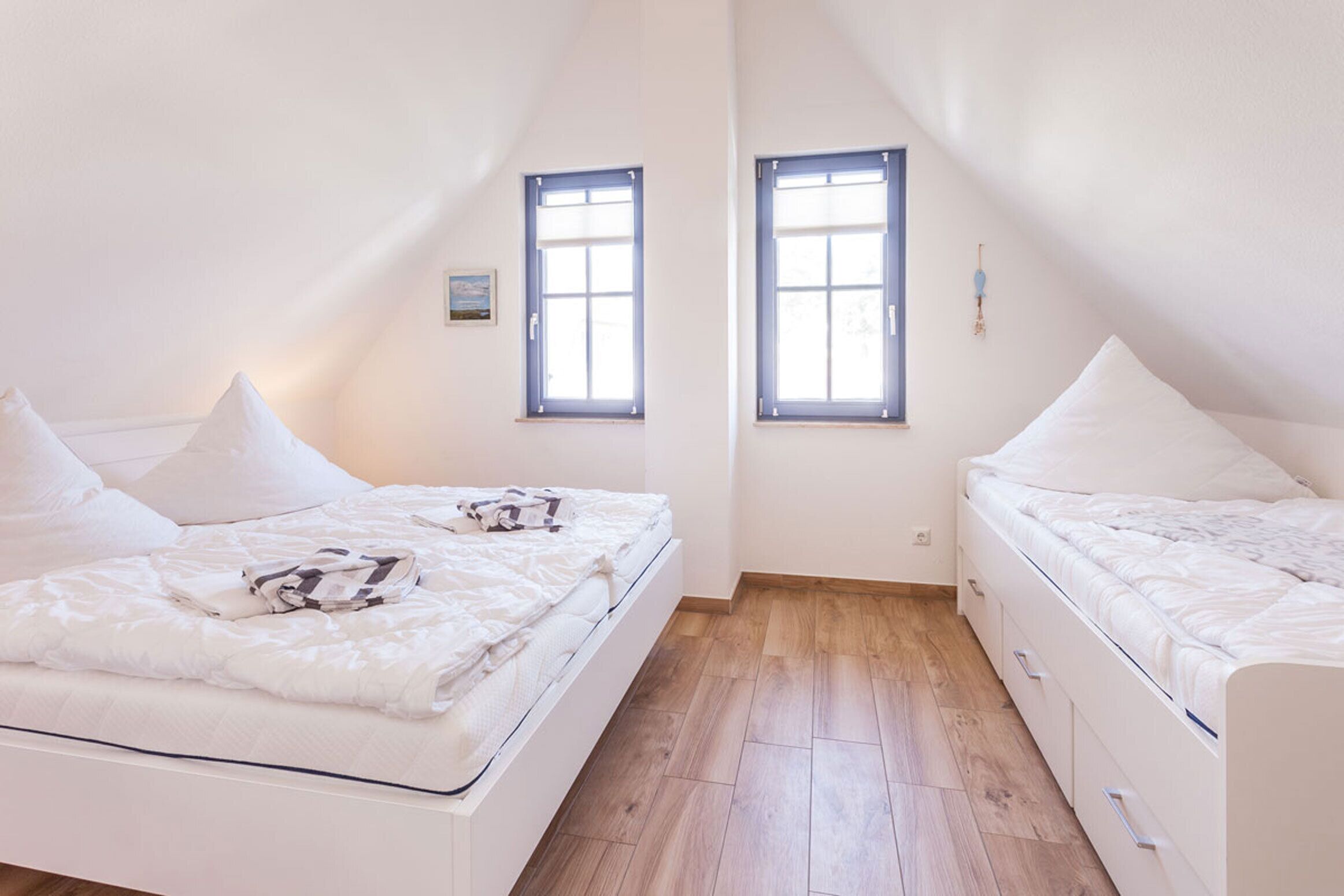 Een slaapkamer met twee bedden, een houten vloer en twee ramen.