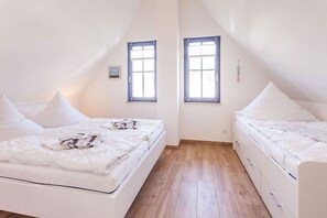 Ein Schlafzimmer mit zwei Betten, Holzboden und zwei Fenstern.
