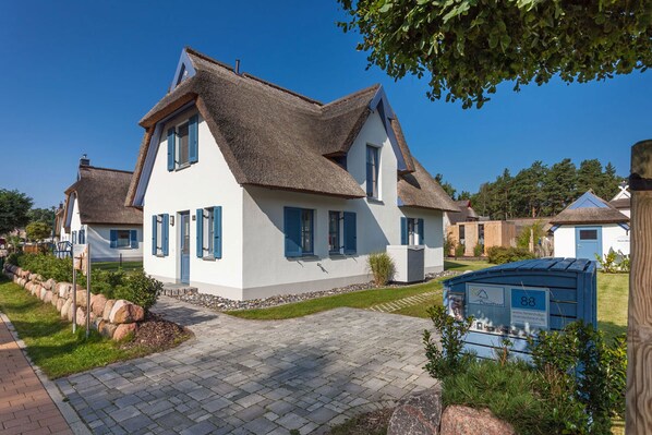 Ein traditionelles Haus mit Strohdach, weißen Wänden und blauen Fensterläden.