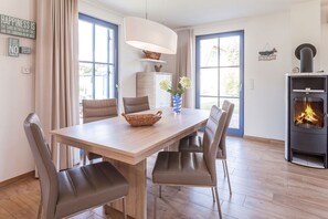 A dining area with a wooden table, four chairs, a vase with flowers, and a fireplace. - Vacation home with a fireplace and sauna, about 500 meters from the sandy beach; dogs are welcome (Glowe)