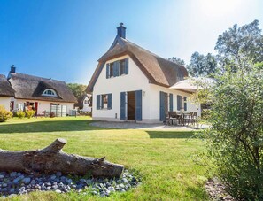Ein traditionelles Haus mit Strohdach, einem gepflegten Rasen und einem Essbereich mit Gartenmöbeln.