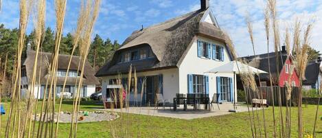 A traditional house with a thatched roof, a front porch with a table and chairs, and a well-maintained lawn.