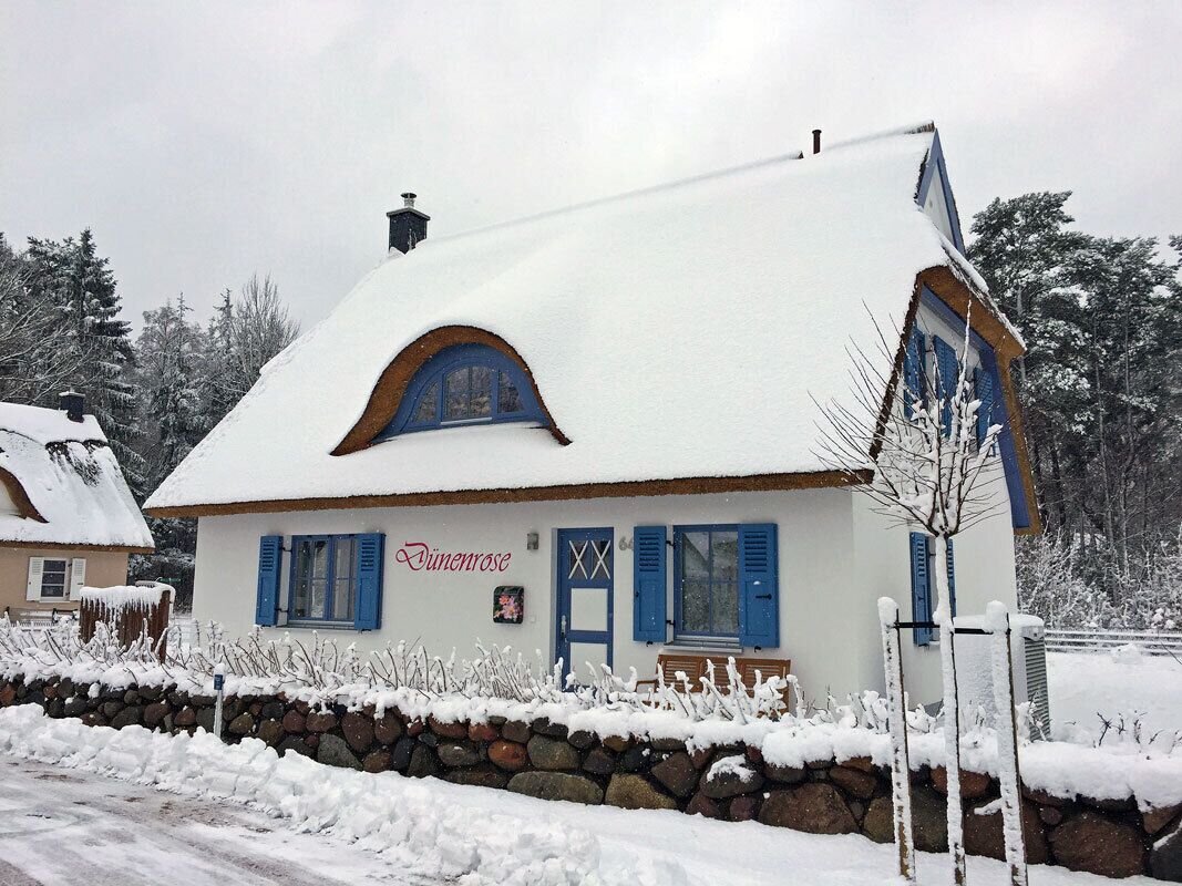 Une maison recouverte de neige, avec un mur de pierre à l’avant, une porte bleue et une cheminée.