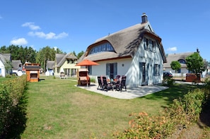 A house with a thatched roof, a patio with outdoor furniture, and a well-maintained lawn. - Vacation home with a fireplace and sauna, about 500 meters from the sandy beach, Wi-Fi, and a washing machine (Glowe)