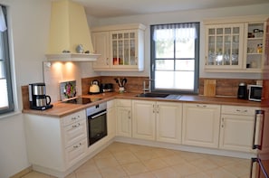 A kitchen with white cabinetry, a built-in oven, a coffee maker, and a window with a view. - Vacation home with a fireplace and sauna, about 500 meters from the sandy beach, Wi-Fi, and a washing machine (Glowe)