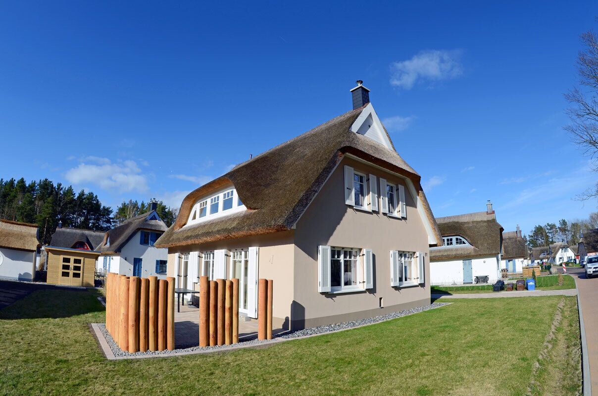 A traditional house with a thatched roof, white walls, and a wooden fence.