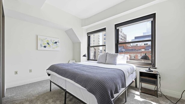 Une chambre avec un lit, un bureau, une lampe, une fenêtre et une vue sur la ville.