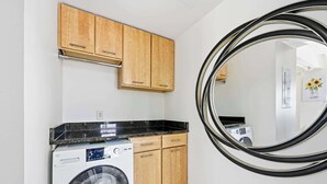 Une buanderie équipée d’un lave-linge, de meubles en bois et d’un grand miroir.