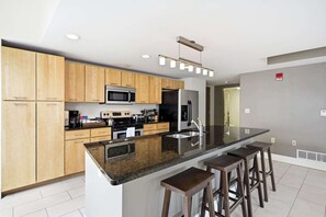A modern kitchen with wooden cabinets, a central island with bar stools, stainless steel appliances, and recessed ceiling lighting. - Modern Loft Living in Downtown Detroit (Detroit)