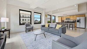 Un salon moderne avec un canapé gris, une petite table ronde et un coin bar avec des tabourets.